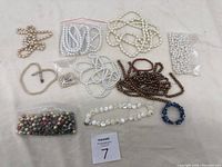 Overview of assorted beads and pearl-style necklaces including multiple colors and types shown on a white fabric background.