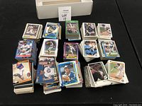 Box and multiple piles of used baseball cards laid out on a black table, showing a variety of players and card designs.