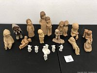 Wide view of entire lot of fifteen assorted clay and ceramic figurines arranged in rows on black surface