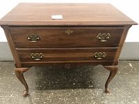 Front view of the wooden desk table showing two drawers with brass handles and cabriole legs.