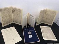 Full view of all historical document reproductions including booklet, printed sheets, and folded handwritten replicas arranged on a flat surface.