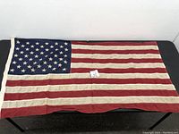 Full view of the flag laid flat showing the entirety of the stars and stripes pattern against a black surface.