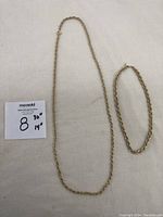 Two gold plated necklaces displayed flat on white surface; one longer 30 inch rope style necklace and one shorter 14 inch rope style choker necklace.