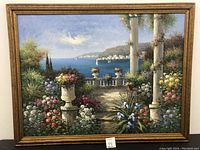 Large framed oil painting showing a colorful garden scene with flowers, urns, columns, and a seaside town in the background