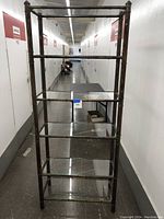 Side view of the tall metal shelving unit showing five clear glass shelves and brass finish metal frame.