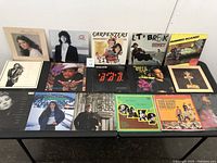 Photo of 15 vinyl records laid out, showing various album covers including Amy Grant, The Carpenters, Sidney, Running Scared soundtrack, and others.