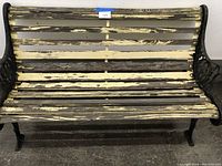 Front view of vintage outdoor bench showing peeling paint on wooden slats and black metal frame with ornate detailing.