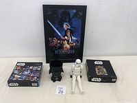Photo of framed Return of the Jedi poster, two Star Wars puzzles in their boxes, Stormtrooper action figure, and Darth Vader helmet mug.