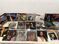 Photo showing full front view of all 20 vinyl record album covers laid out on a table, depicting varied artists and styles.