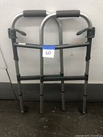Front view of the aluminum folding walker with two front wheels and padded gray handles showing adjustment mechanisms and labels.
