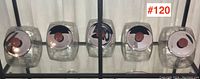 Five clear glass candy jars with black and red lids lined up on a shelf, showing varied angles of lids and jar shapes.