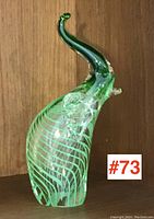 Side view of the green and clear art glass elephant with raised trunk and white stripes.