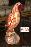 Front view of the red and yellow swirled art glass parrot perched on a clear glass base.