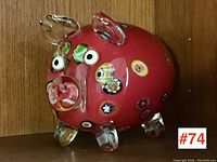 Front-right angled view of red art glass pig showing colorful embedded millefiore floral details, clear glass ears, eyes, and snout, clear feet.