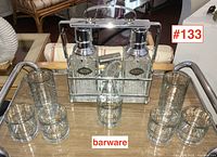 Wide view showing tantalus with two decanters and seven glasses arranged around it on a table.