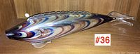 Full view of large elongated fish glass sculpture showing fenicio multicolored swirls and clear glass fin.