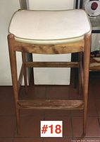 Front view of mid-century modern teak bar stool showing white cushioned seat and teak legs with footrest.