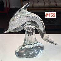 Clear glass dolphin figure with internal bubbles on a glass base observed from the front and right side.