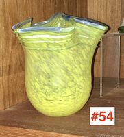 Front view of small yellow spatter glass vase with ruffled clear rim, showing mottled pattern and shape.