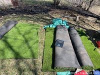 Three outdoor astroturf carpet pieces shown outside on grass. Two pieces lay flat; one is rolled up. Green turf surface with black backing visible.