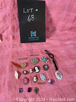 Multiple vintage brooches arranged on pink cloth, showing variety of styles including cameos, floral porcelain, rhinestones, and stones.