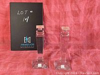 Pair of crystal taper candle holders with original seal on square base, set against red fabric backdrop with black box behind.