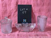 Front view of three crystal pieces: ice bucket with lid, oval bowl, and tall vase with scalloped edges on a pink background.
