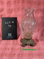 Front view of the large crystal vase with intricate cut designs and metal base against a red fabric background alongside a black sign showing lot number.