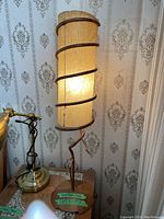 Full view of the lamp showing tall cylindrical lighted leather shade with dark leather cord spiraled around, standing on a carved teak base.