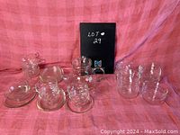 Photo of the entire glass teapot set including teapot, cups, saucers, and bowls arranged on cloth background.