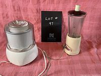 Photo showing vintage electric ice cream maker with metallic top and blender with glass jar, both plugged in and on a pink cloth background.