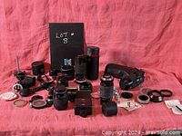 Wide view of entire assortment of lenses, flashes, and camera accessories displayed on pink cloth.