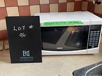 White RCA microwave oven showing front view with control panel, glass door, and measurements label on top front edge.