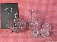 Full view of the crystal lot with jug, lidded candy dish, cream and sugar set, and small candy dish displayed on a pink cloth background.