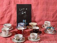 Ten assorted vintage teacups and saucers arranged in two rows with a black sign displaying lot number 64