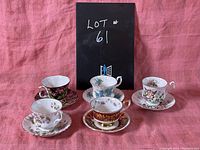 Photo showing five Royal Albert teacups and saucers arranged on a pink fabric surface with lot number card in background.