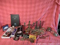 Wide view of assortment of vintage silver plated items including candle holders, trays, cream pitcher, serving tongs, ladle, and small bowls with tarnish visible.