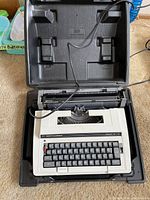 Electric Smith Corona typewriter inside black hard plastic carrying case with power cord visible.