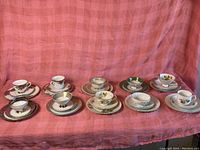 Wide view of 9 assorted porcelain tea cup and matching saucer sets arranged in a row.