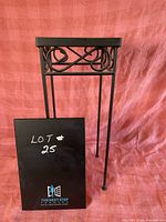 Full view of the tile and metal table against a pink cloth background, showing the entire metal frame with decorative scrolls under the tile top.