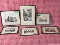 Six framed vintage prints arranged on pink fabric, featuring various European architectural scenes.