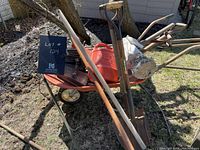 Wide view of wheelbarrow filled with assorted garden tools and accessories such as shovels, rakes, gloves, a watering can, and a decorative statue.