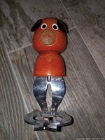 Front view of 1940s pig bottle opener on wooden floor showing the hand-painted wood head and metal opener.