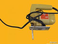 Side view of yellow Black & Decker electric saw with black power cord coiled around handle, showing the blade and base plate.