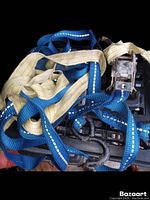 Two different packing straps, one blue and one beige, with metal ratchet buckles and reflective stitching on a black plastic surface.