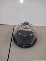 Covered cake plate with glass dome on stone base shown from side angle.