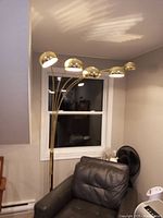 Full view of five-headed brass floor lamp placed beside chair in room.