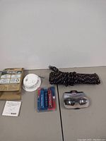 Photo showing First Alert fire alarm with packaging, Tectran HEX-GRIP Gladhand Grip Set blue anodized aluminum grips in packaging, a large coil of black rope with red/white accents, and smaller items arranged on a table.