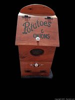 Front view of wooden storage box with 'Potatoes & Onions' painted on hinged lid, featuring mesh vent and knob on front panel.