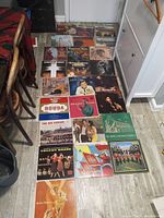 Photo showing about 20 vinyl record album covers arranged on floor. Variety of music genres and artists including Jackie Gleason, Chris Connor, Sousa, and military band albums.